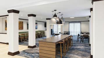 Eine moderne Hotelhalle mit einer zentralen Bar, Sitzgelegenheiten und einem großen Fenster, das für natürliches Licht sorgt.