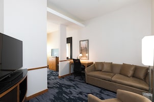 A hotel room with a flat-screen TV, a sofa, a desk, and a chair.