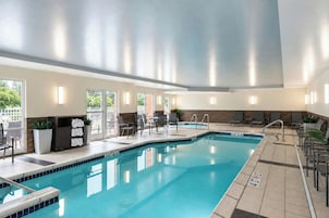 A swimming pool with a tiled edge, a lounge area with chairs and tables, and a view of the outdoors through large windows.