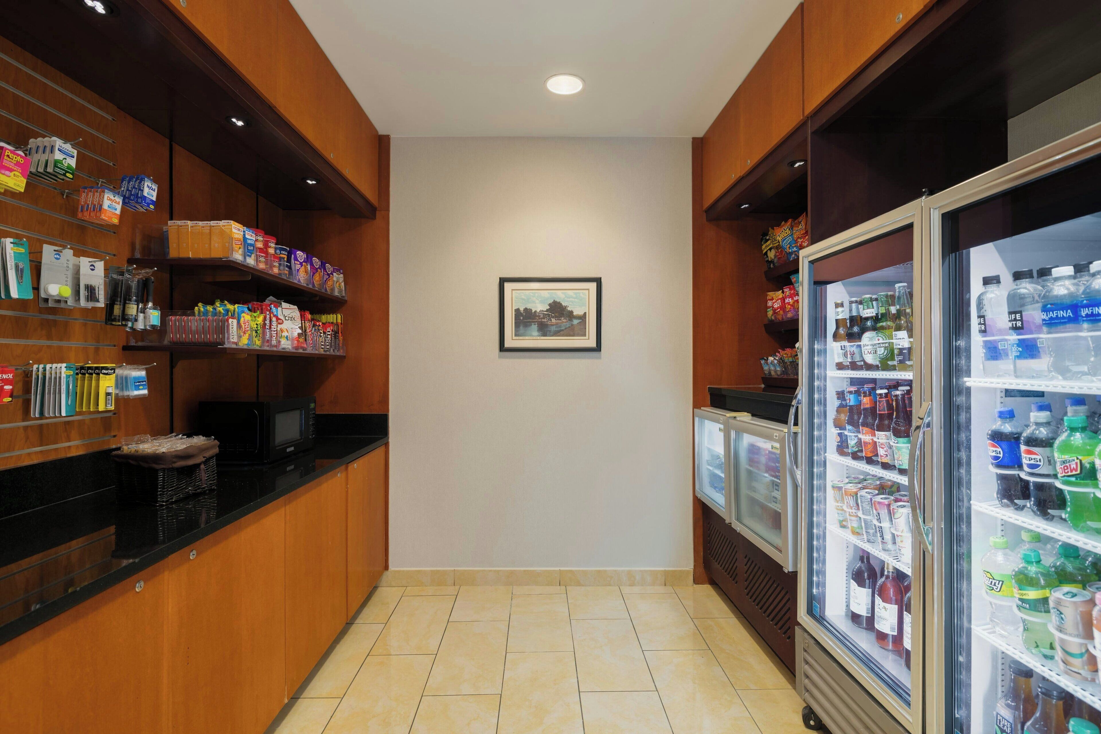 A hotel kitchenette with wooden cabinets, a microwave, and a refrigerator stocked with beverages.