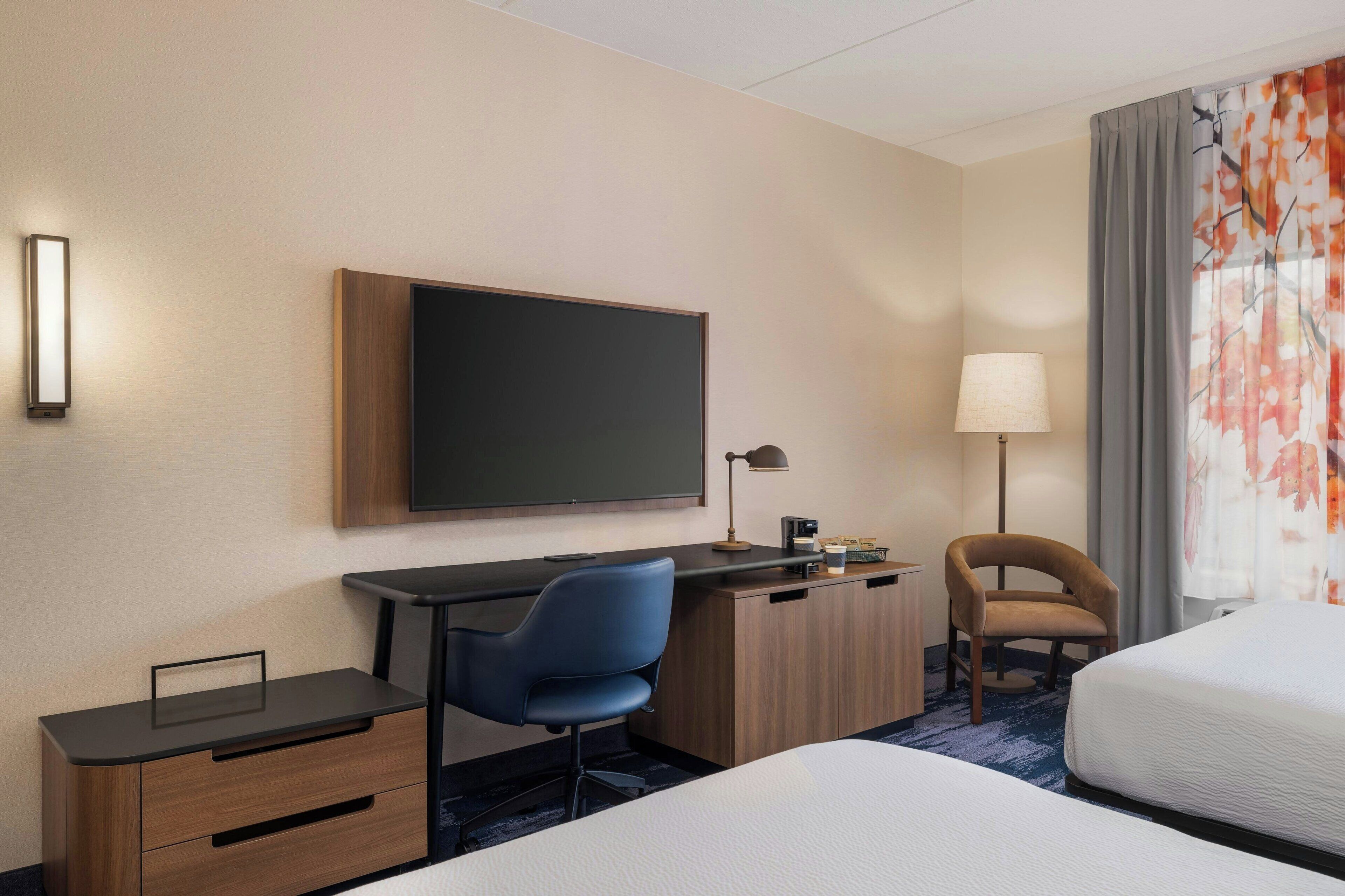 A hotel room with a bed, a desk with a chair, a flat-screen TV, a lamp, and a coffee maker.