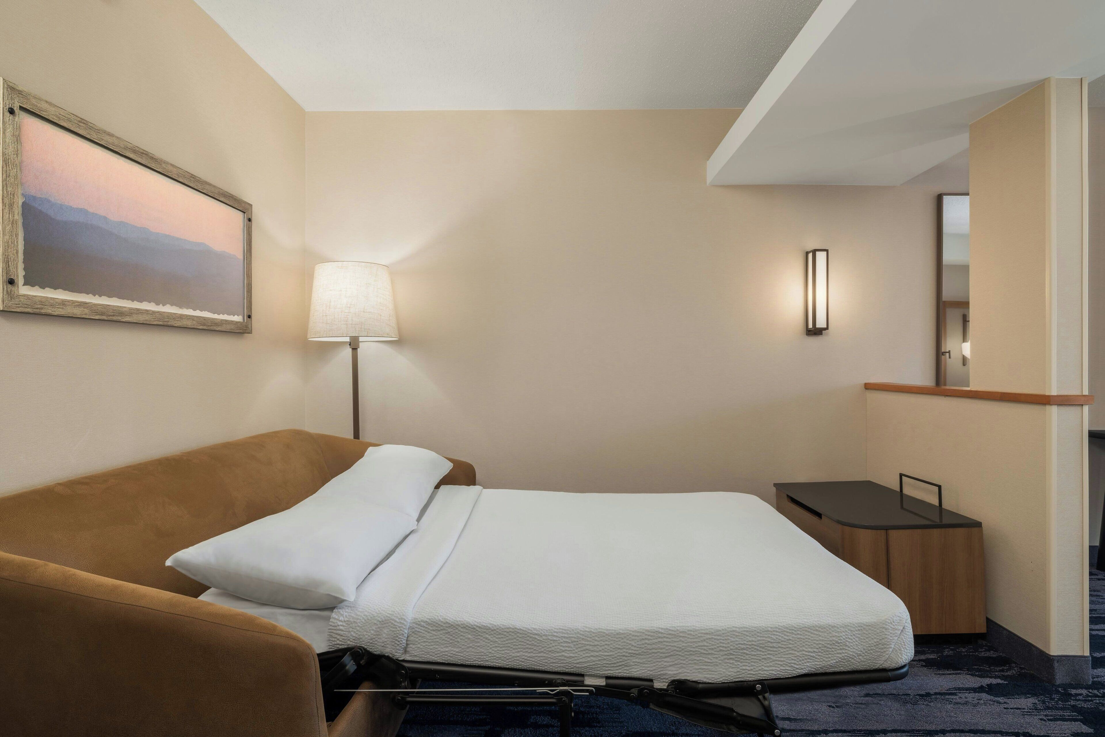 A hotel room with a bed, a sofa, a desk, a lamp, and a painting on the wall.