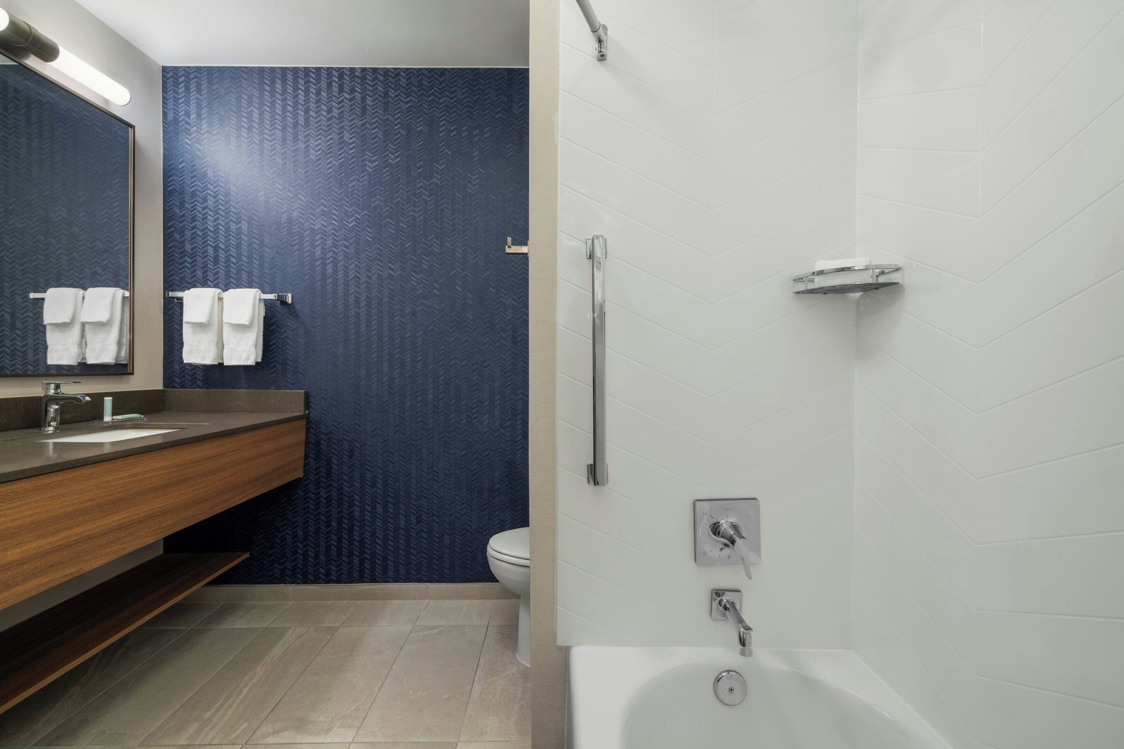A modern bathroom with a wooden vanity, a large mirror, a white bathtub, and a blue textured wall.