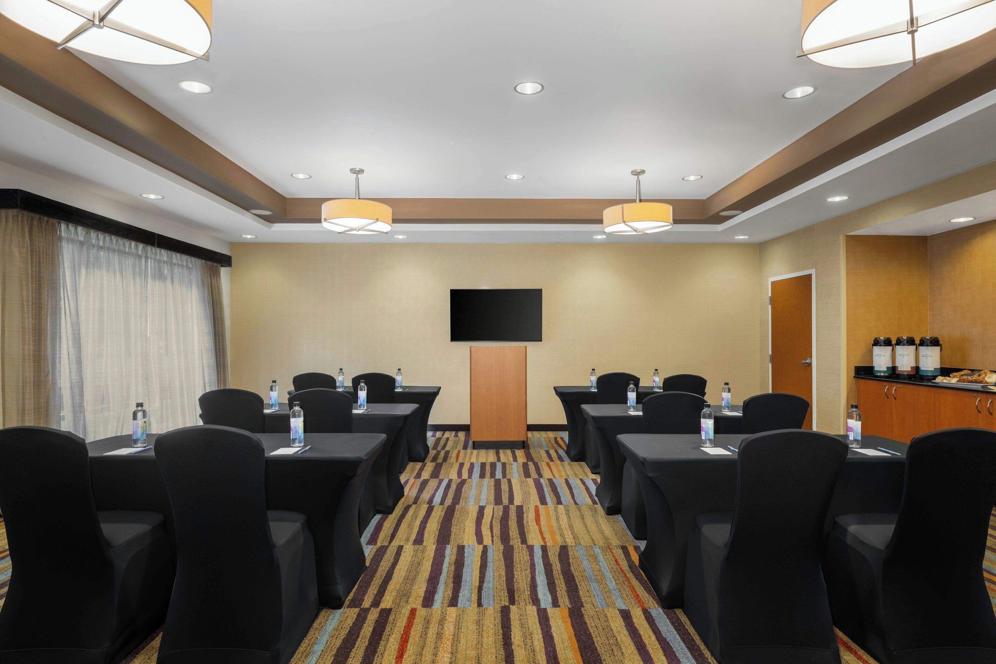 A conference room with tables, chairs, a flat-screen TV, and a minibar.