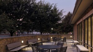 Een terras buiten met ronde tafels en stoelen, banken en een stenen muur.
