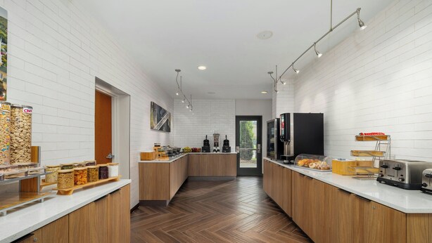 Een moderne keuken met witte bakstenen muren, houten kastjes en een visgraatvloer. Op de aanrecht staan diverse etenswaren en apparaten.