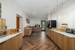 A modern kitchen with white brick walls, wooden cabinets, and a herringbone floor. There are various food items and appliances on the countertops.