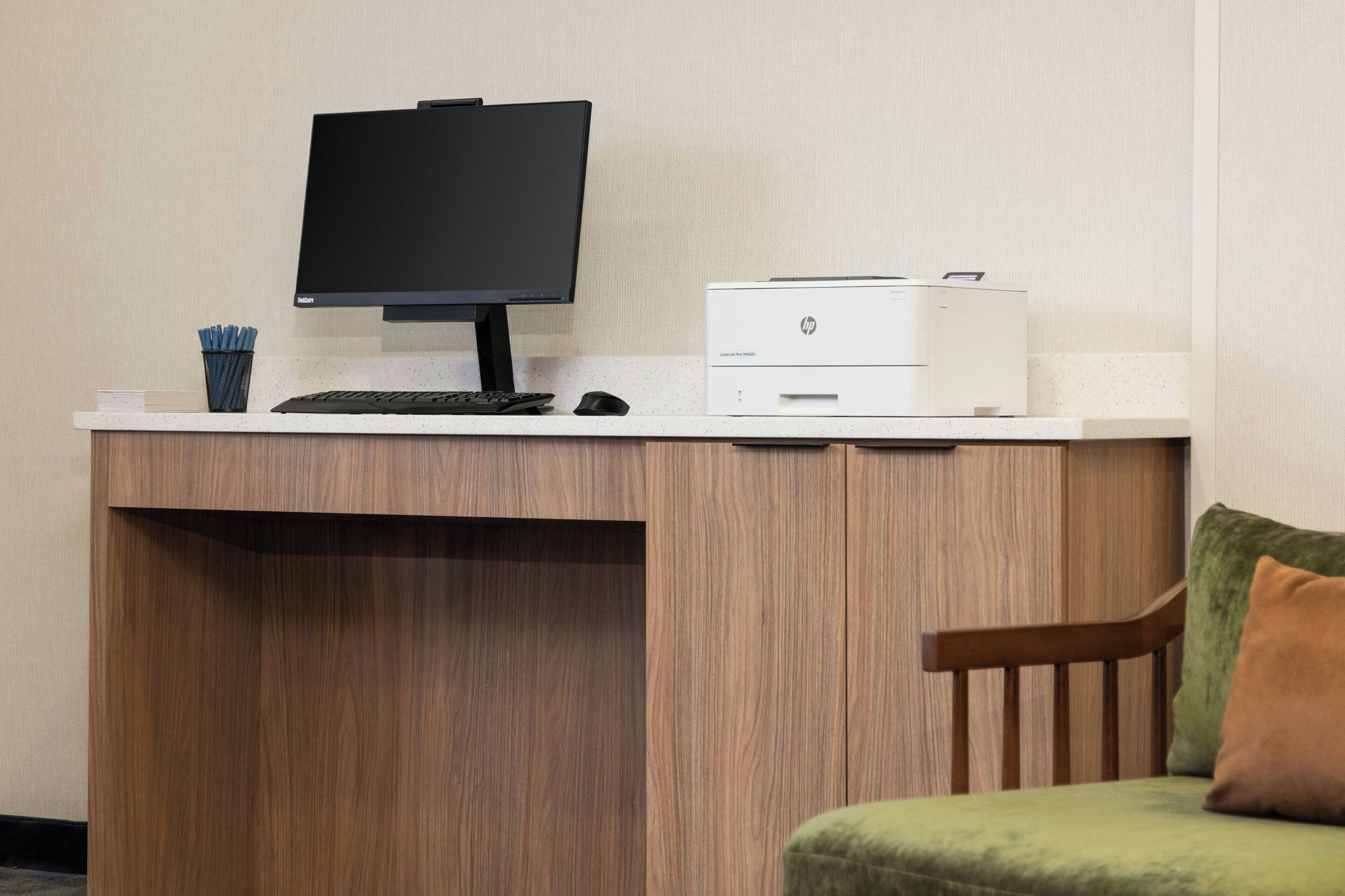 Un escritorio de madera con un monitor de computadora, teclado, ratón e impresora HP.