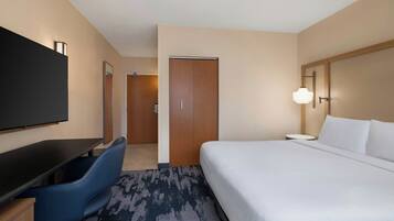 A hotel room with a bed, a desk with a chair, a television, and a door.