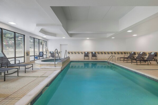 An indoor swimming pool with lounge chairs and a hot tub.