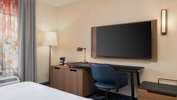 A hotel room with a bed, a desk with a chair, a flat-screen TV, a lamp, and a wardrobe.