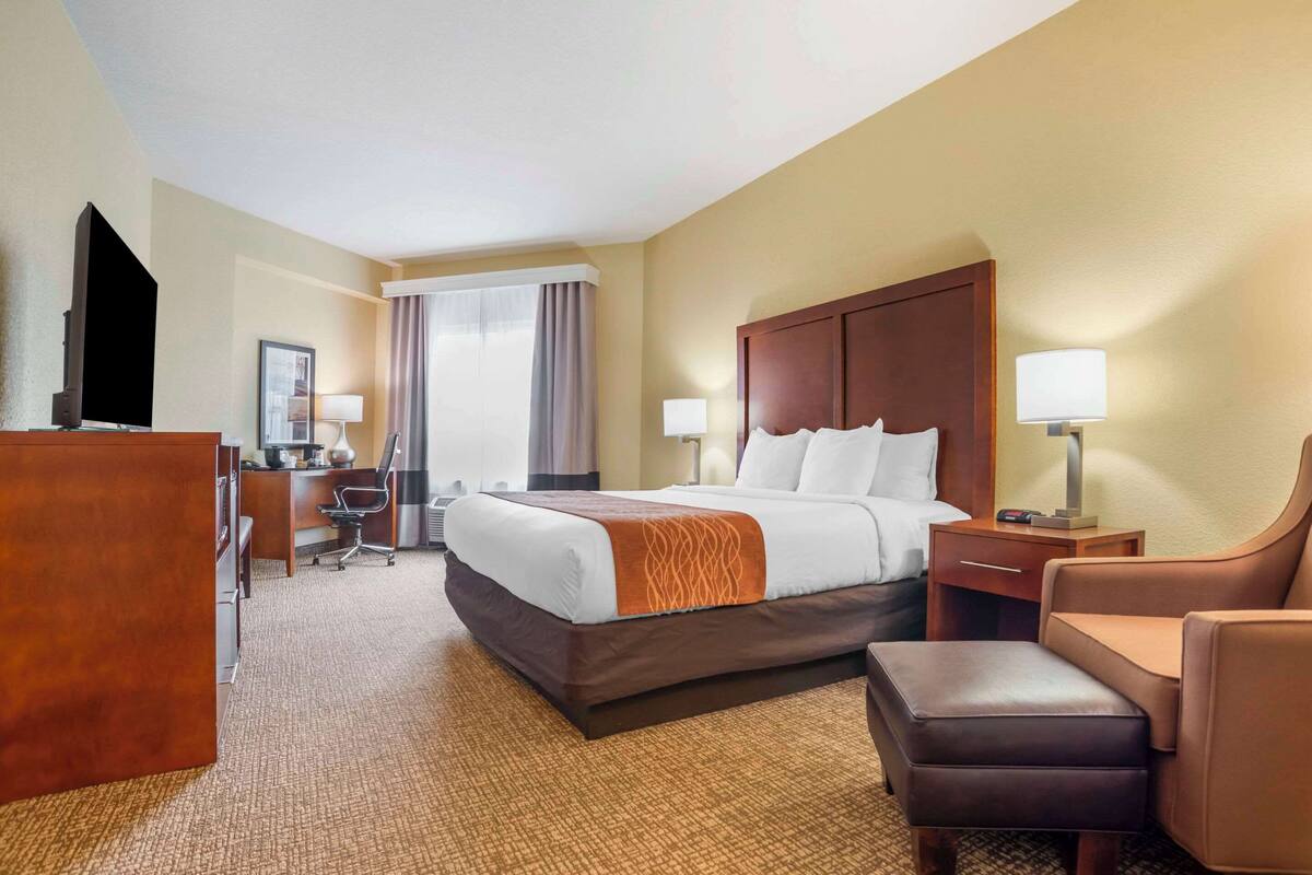 A hotel room with a large bed, a desk, a chair, a TV, and a window with curtains.