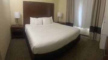 A hotel room with a large bed, two bedside tables with lamps, a headboard, and a window with curtains.