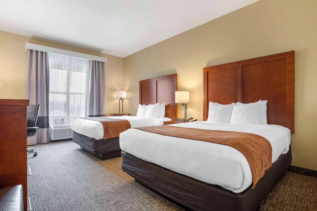 A hotel room with two beds, a desk, a chair, and a large window with curtains.