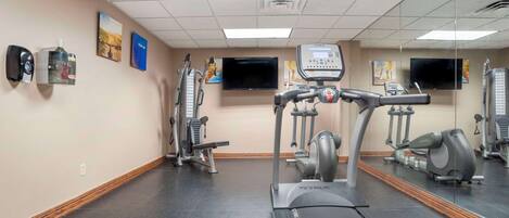 Et fitnesscenter med løbebånd, motionscykler og styrkemaskiner. Der er spejle på væggene og et fjernsyn.