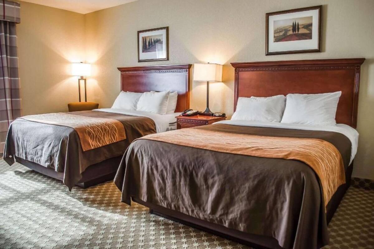 A hotel room with two beds, each with a wooden headboard, bedside tables, lamps, and framed pictures on the wall.