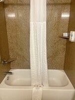 Un baño con bañera, cortina de ducha y un estante con artículos de aseo.