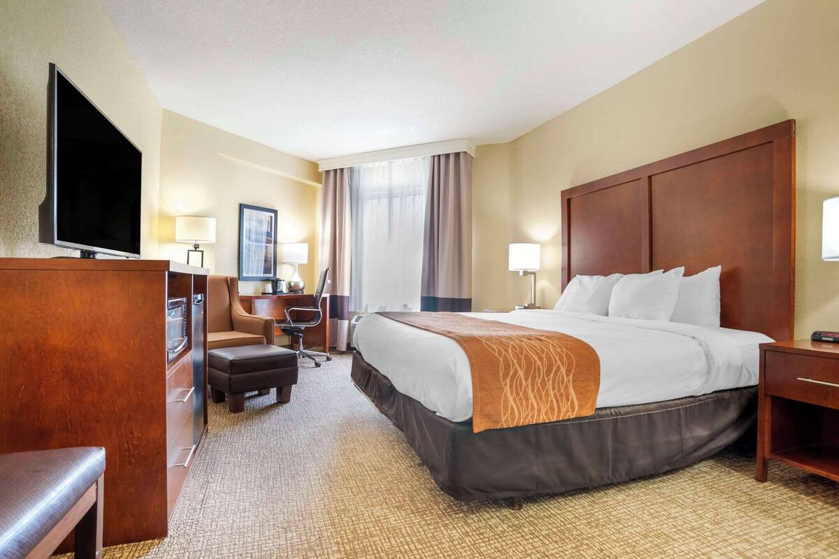 A hotel room with a large bed, a desk, a chair, a television, and a flat-screen TV mounted on the wall.