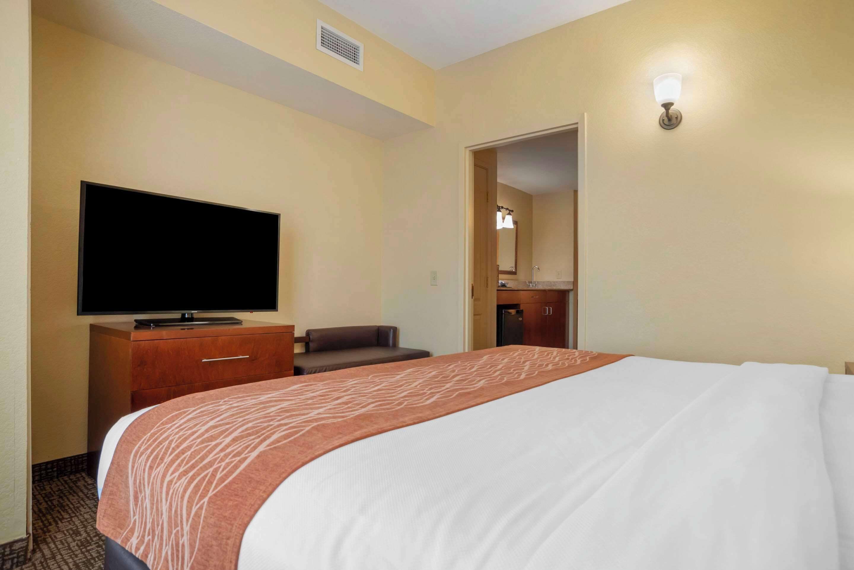 Ett hotellrum med en stor säng, en platt-TV, ett skrivbord med en stol, ett litet pentry och ett badrum som syns genom en öppen dörr.