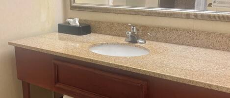 A bathroom with a granite countertop sink, a mirror, and a towel rack.