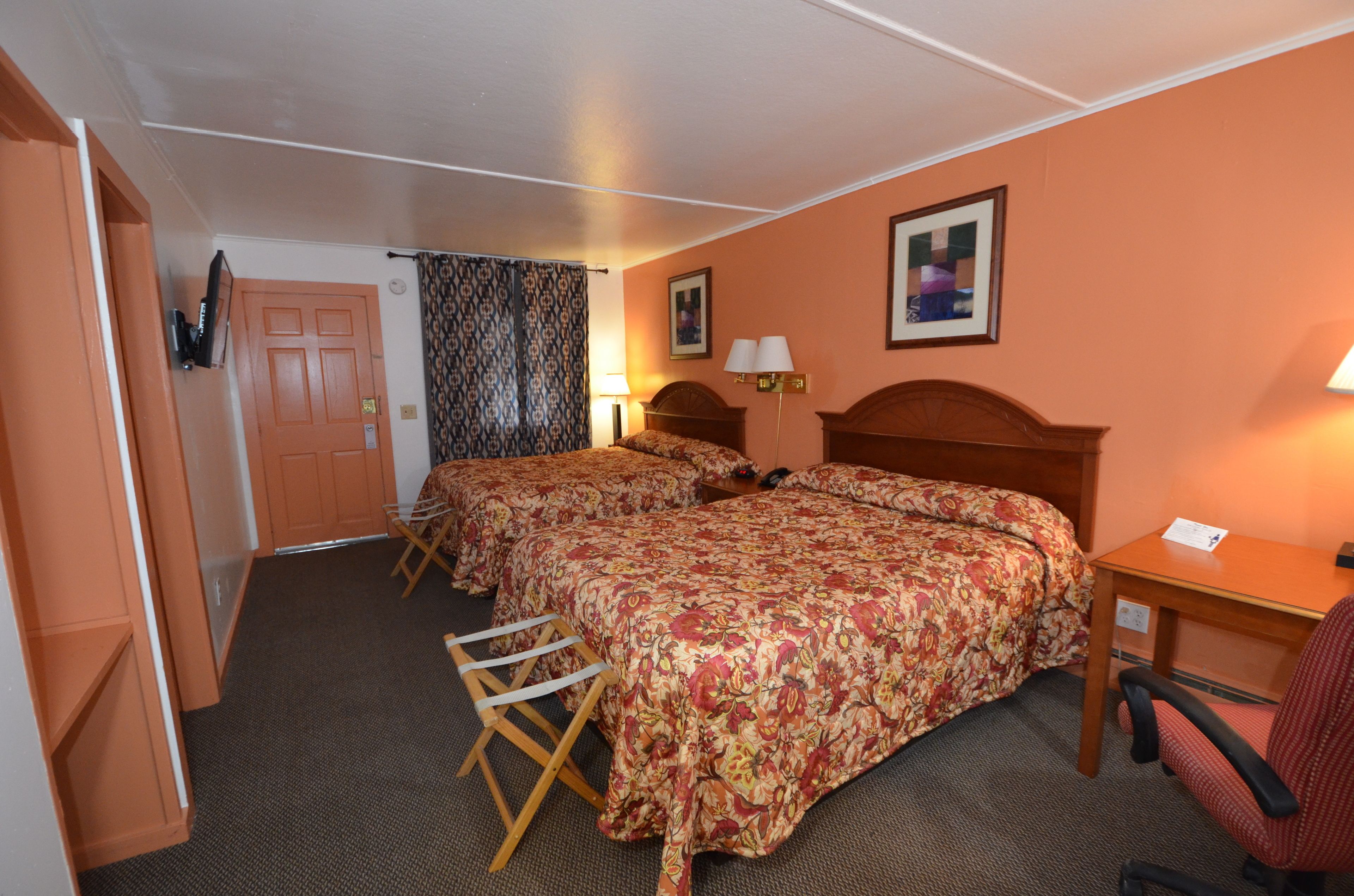 A hotel room with two beds, a desk, a chair, a lamp, and a curtain.