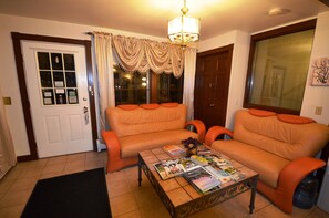 A living room with a sofa, a coffee table with magazines, a door, and a window with curtains. - Williamstown Motel (Williamstown)