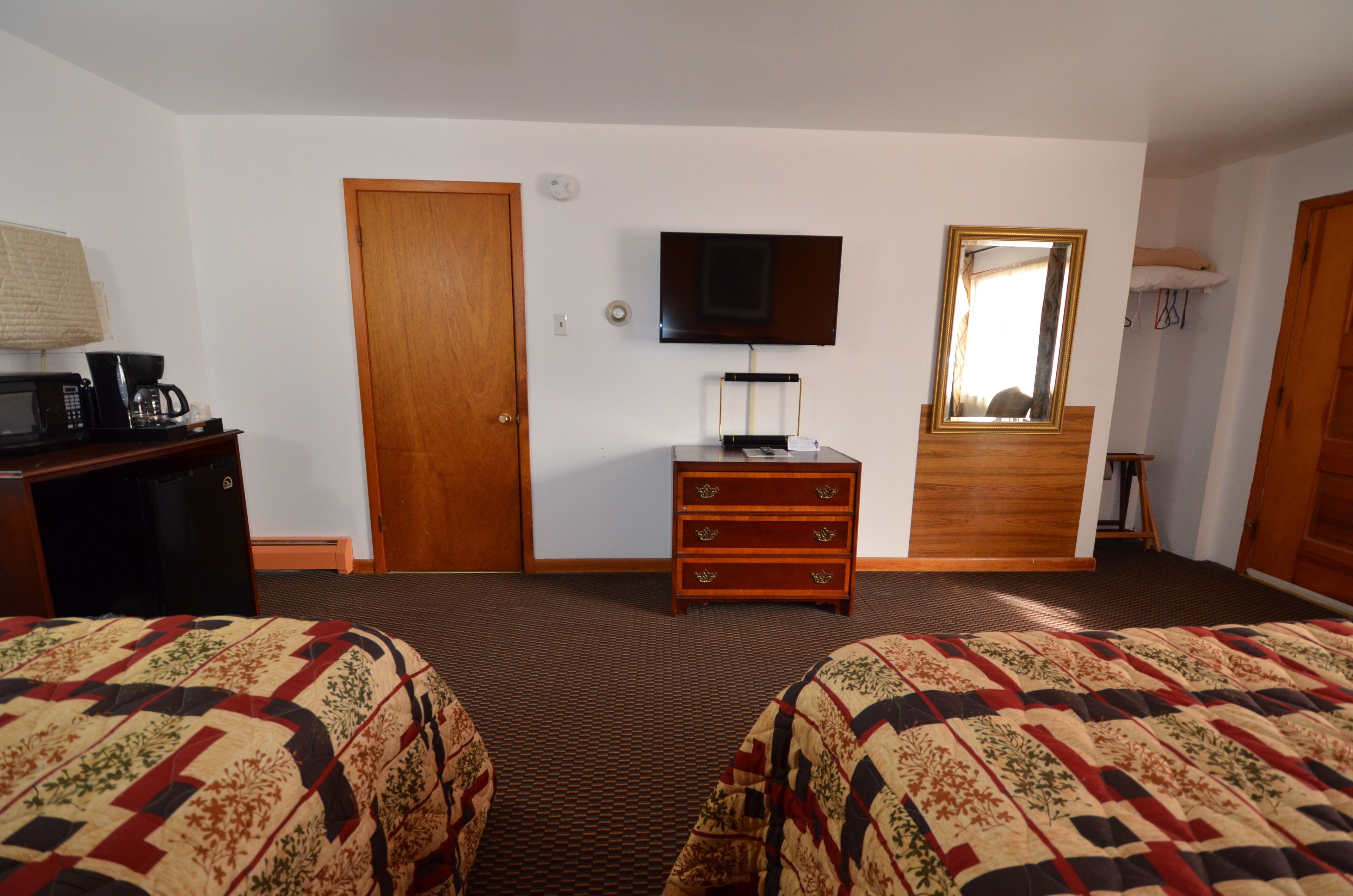 A hotel room with two beds, a TV, a dresser, and a mirror.