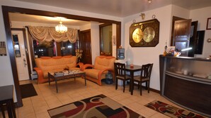 A living room with a sofa, chairs, a coffee table, and a rug. There is a kitchen area with a refrigerator and a water dispenser. - Williamstown Motel (Williamstown)