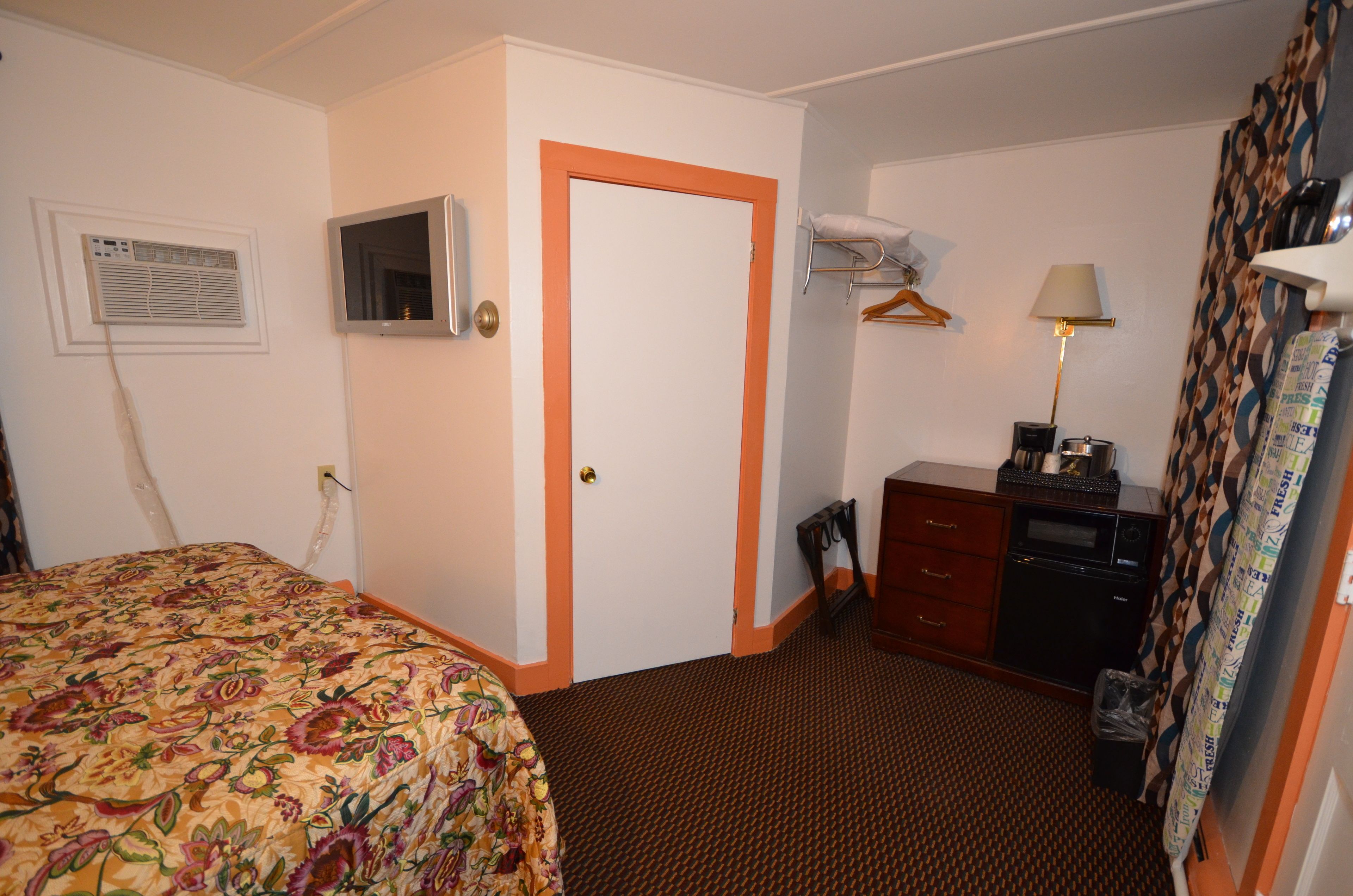 A hotel room with a bed, a dresser, a mirror, a lamp, and a window with curtains.
