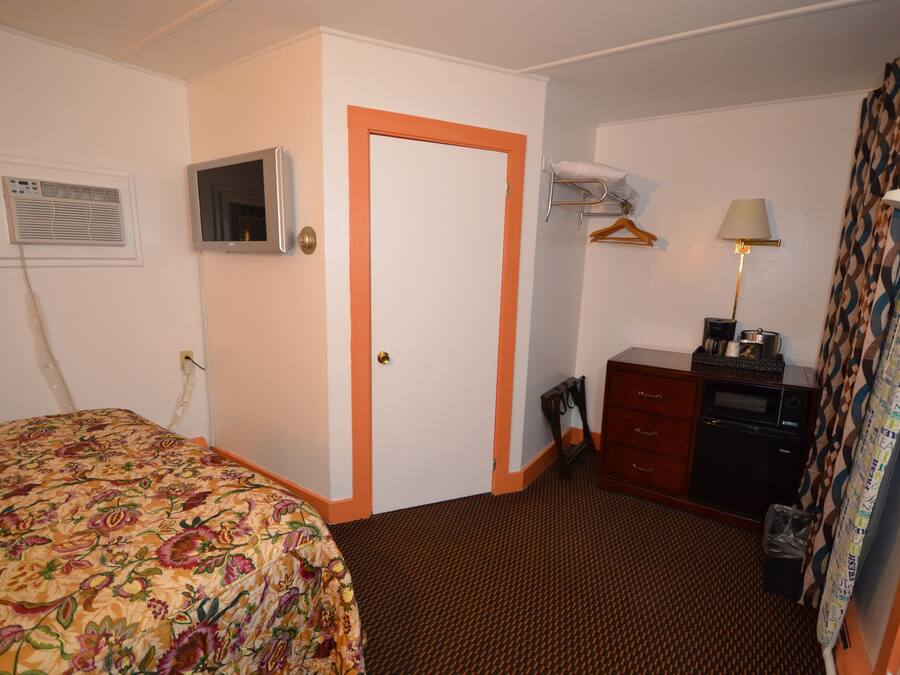 A hotel room with a bed, a dresser, a mirror, a lamp, and a window with curtains.