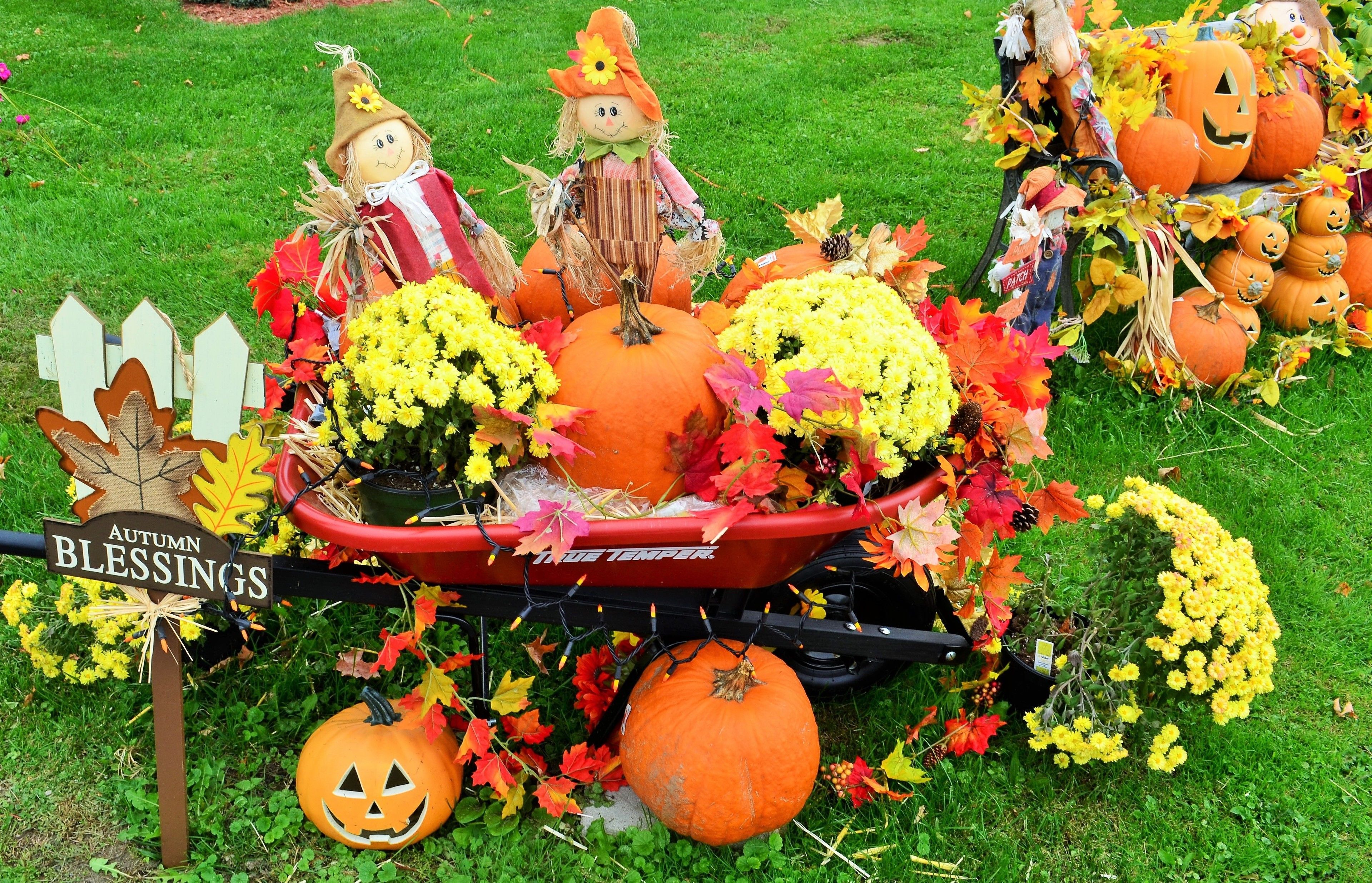 A decorated pumpkin display with a sign reading "AUTUMN BLESSINGS" and a small wagon filled with pumpkins and autumn leaves.