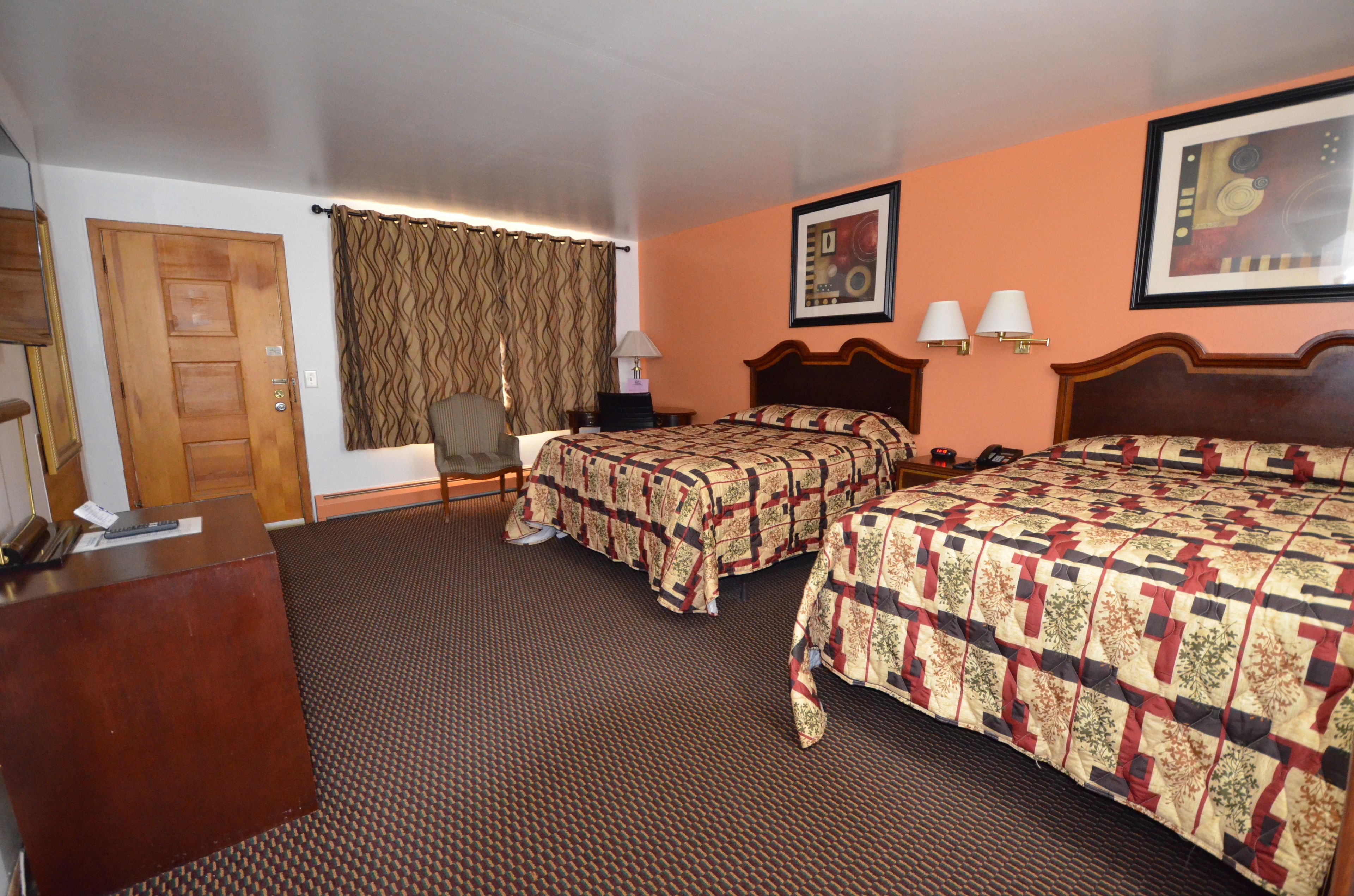 A hotel room with two beds, a desk, a chair, and a door.