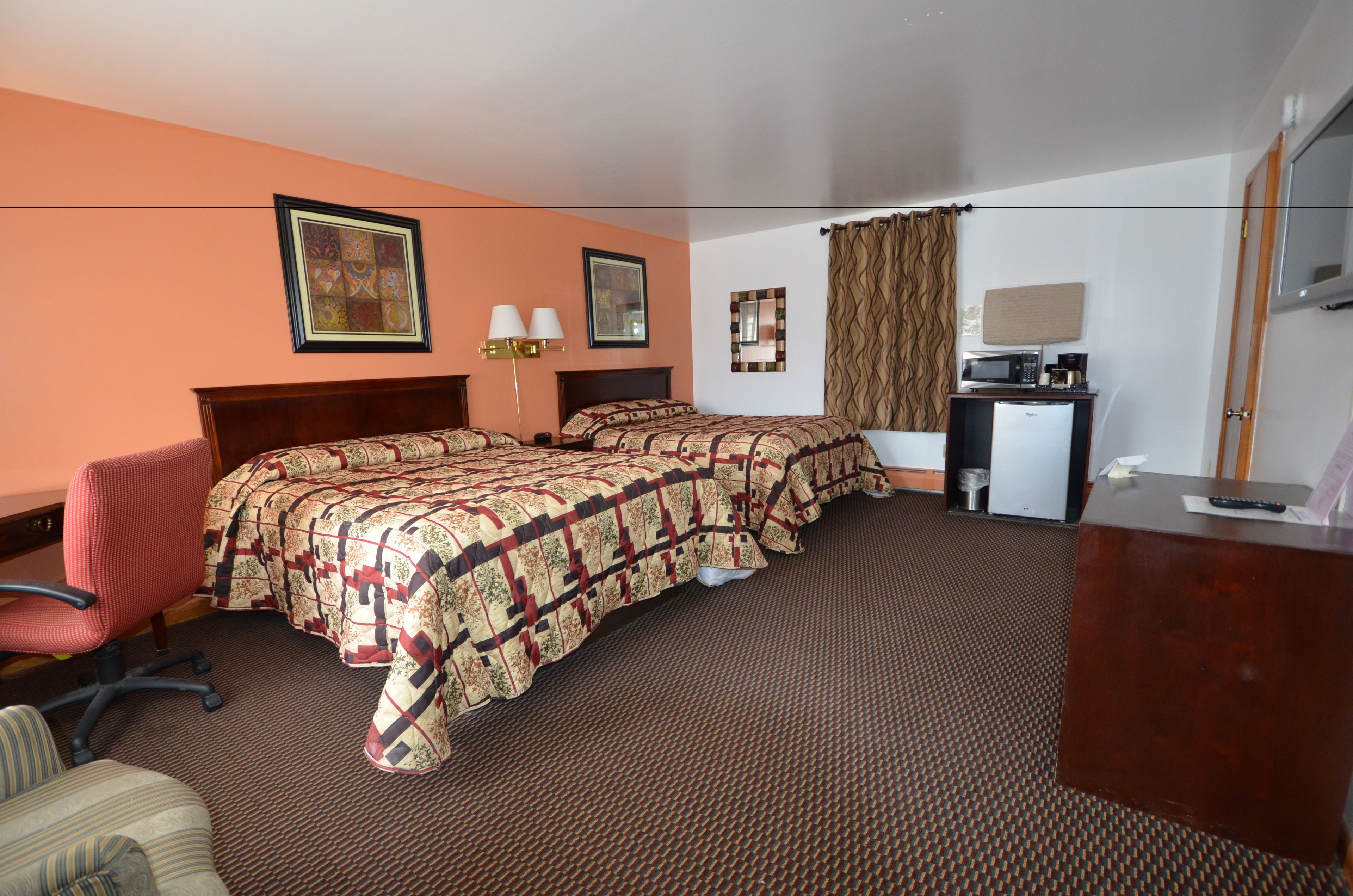A hotel room with two beds, a desk with a microwave, a chair, and a television.