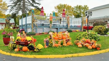 Un espacio exterior decorado con una terraza de madera azul, varias decoraciones de Halloween y un coche rojo aparcado cerca.