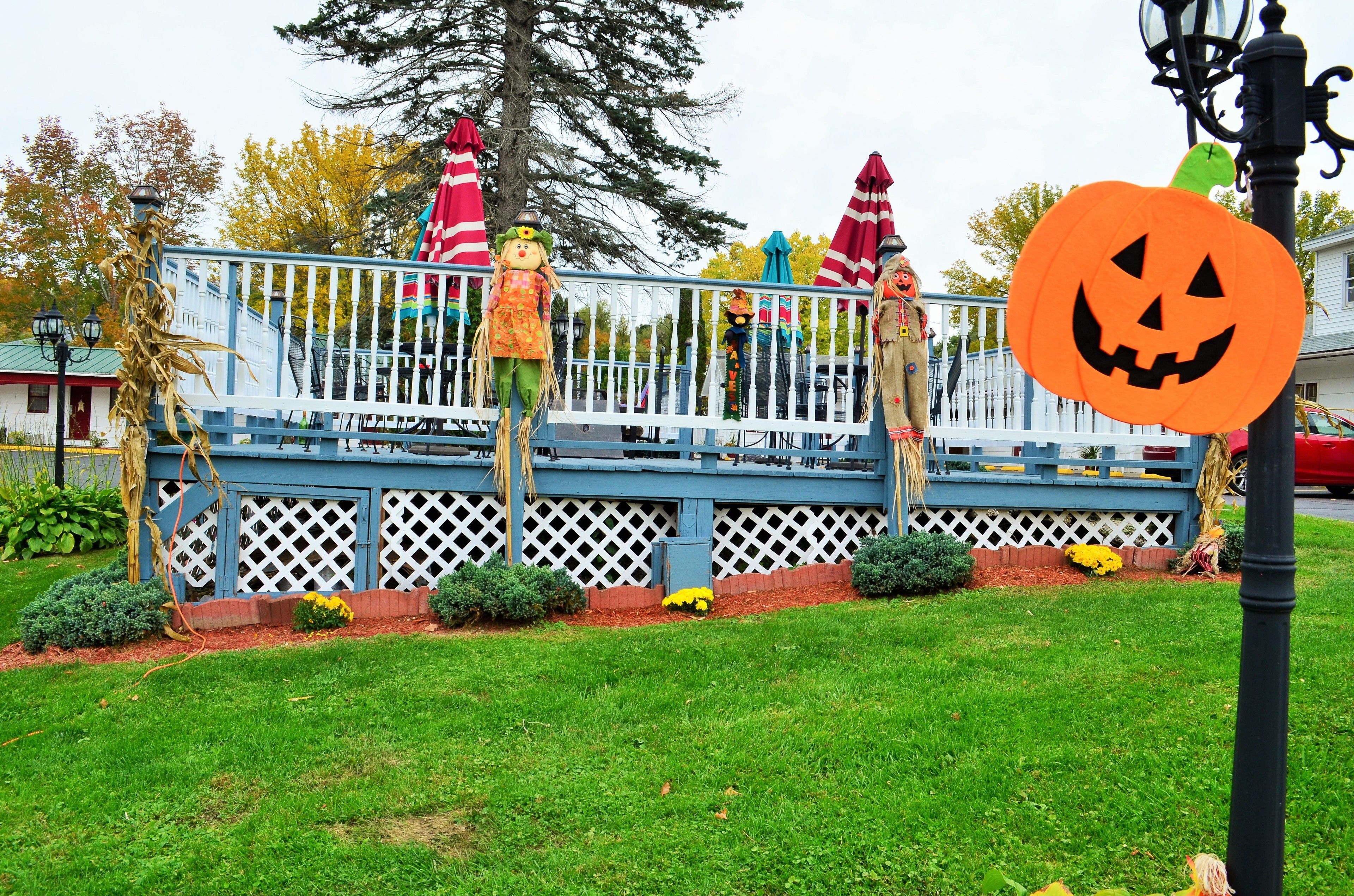 Un deck azul con barandillas de celosía blanca, decorado con figuras de Halloween y un farolillo de calabaza.