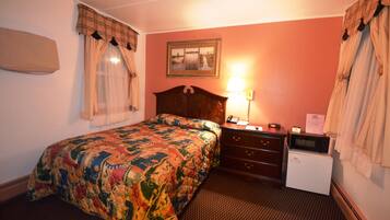A hotel room with a bed, a nightstand, a lamp, a microwave, and a small refrigerator.