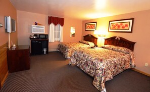 A hotel room with two beds, a desk with a microwave, a trash bin, and a television on the wall. - Williamstown Motel (Williamstown)