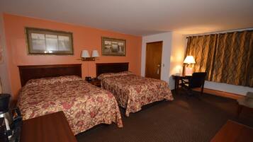 Quarto de hotel com duas camas, uma escrivaninha, uma cadeira, um abajur e uma porta.