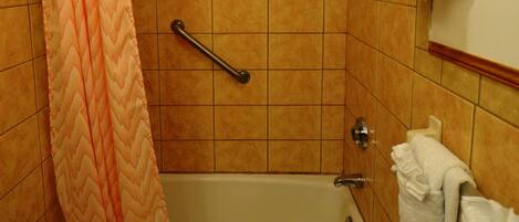 A bathroom with a bathtub, a shower curtain, a grab bar, and multiple towels.