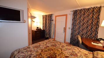 Una habitación de hotel con una cama, un escritorio, una silla, un televisor y una puerta.