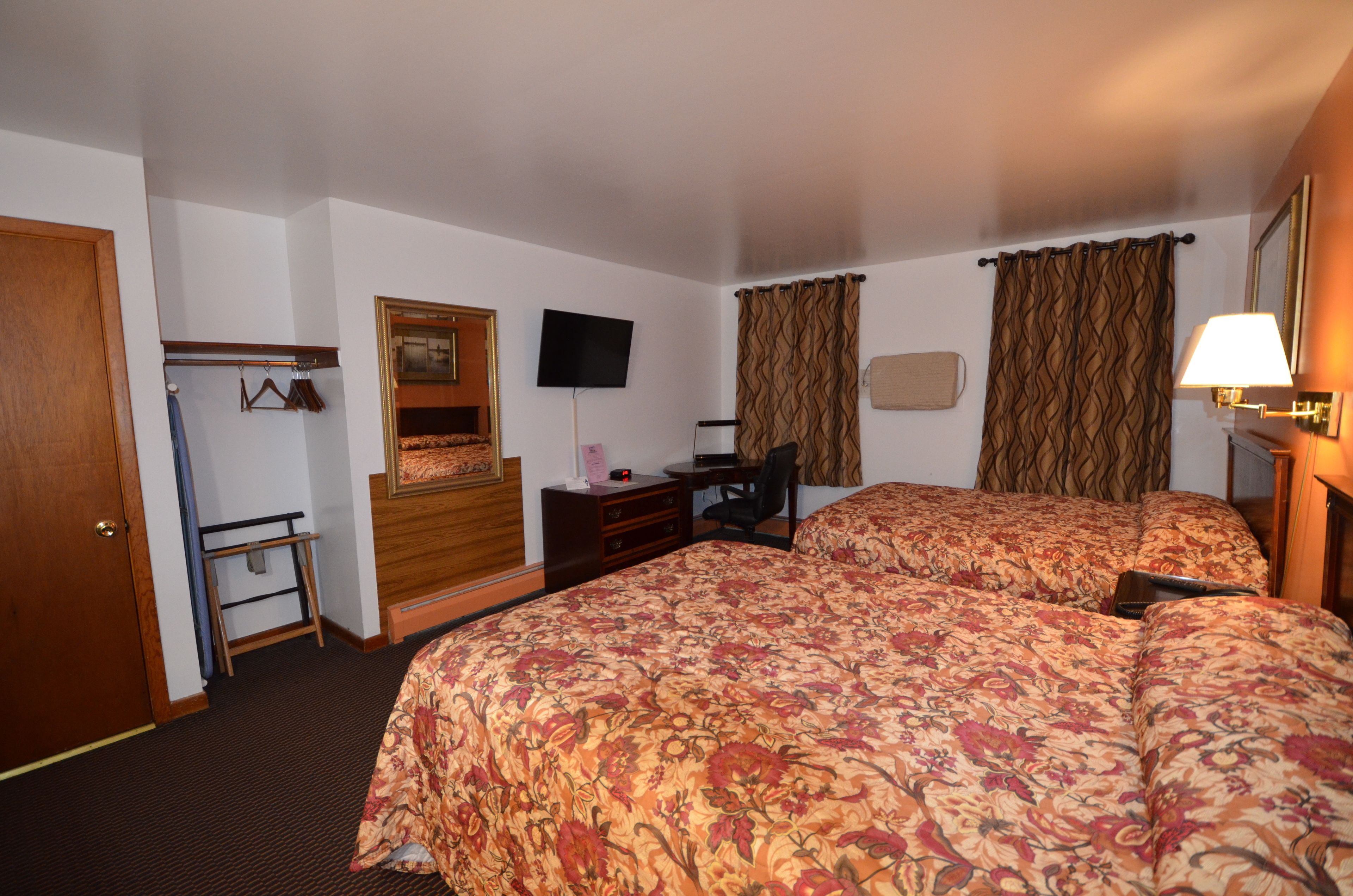 A hotel room with two beds, a desk, a chair, a television, and a wardrobe.