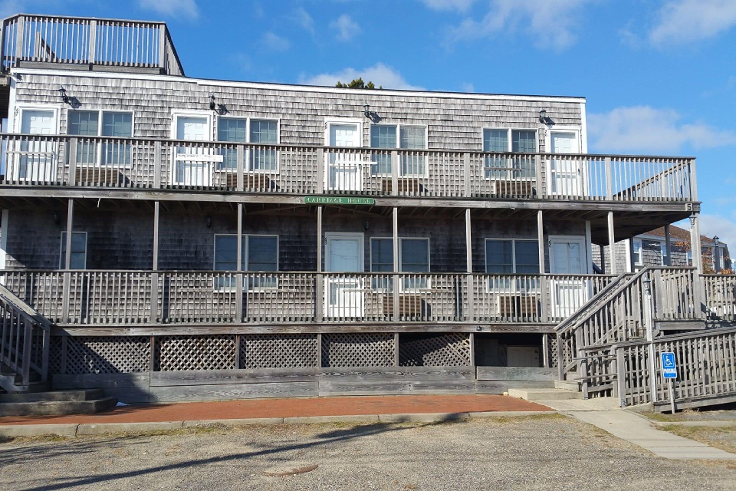 Een gebouw met twee verdiepingen, met een balkon op de bovenste verdieping, een bordje met de tekst 'CAMPING HOUSE' en een gehandicaptenparkeerplaats.