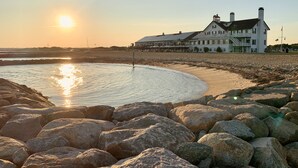 Una propiedad frente a la playa con un edificio grande, una playa de arena y un litoral rocoso.