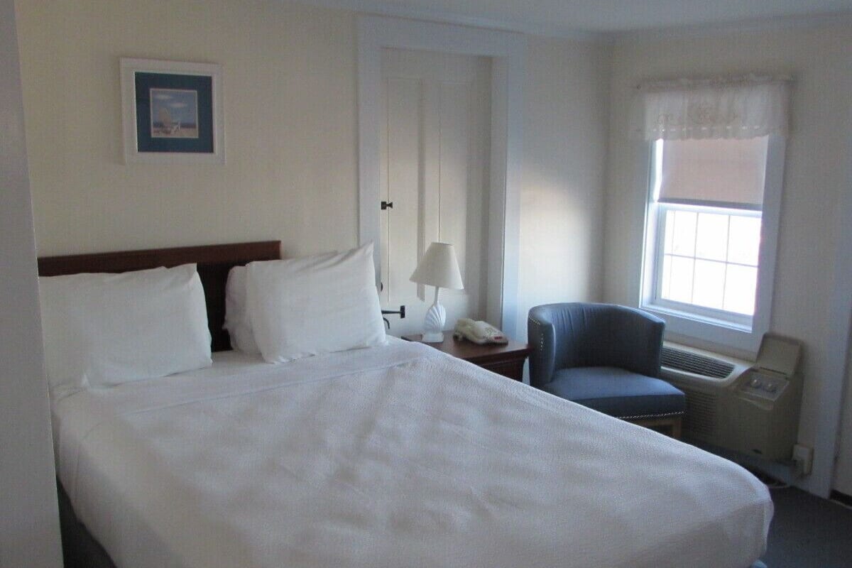 Habitación de hotel con una cama grande, una silla, una mesita de noche, una lámpara y una ventana.