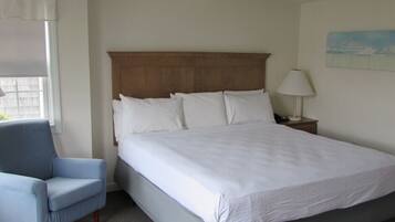 A hotel room with a bed, a chair, a nightstand, and a window.