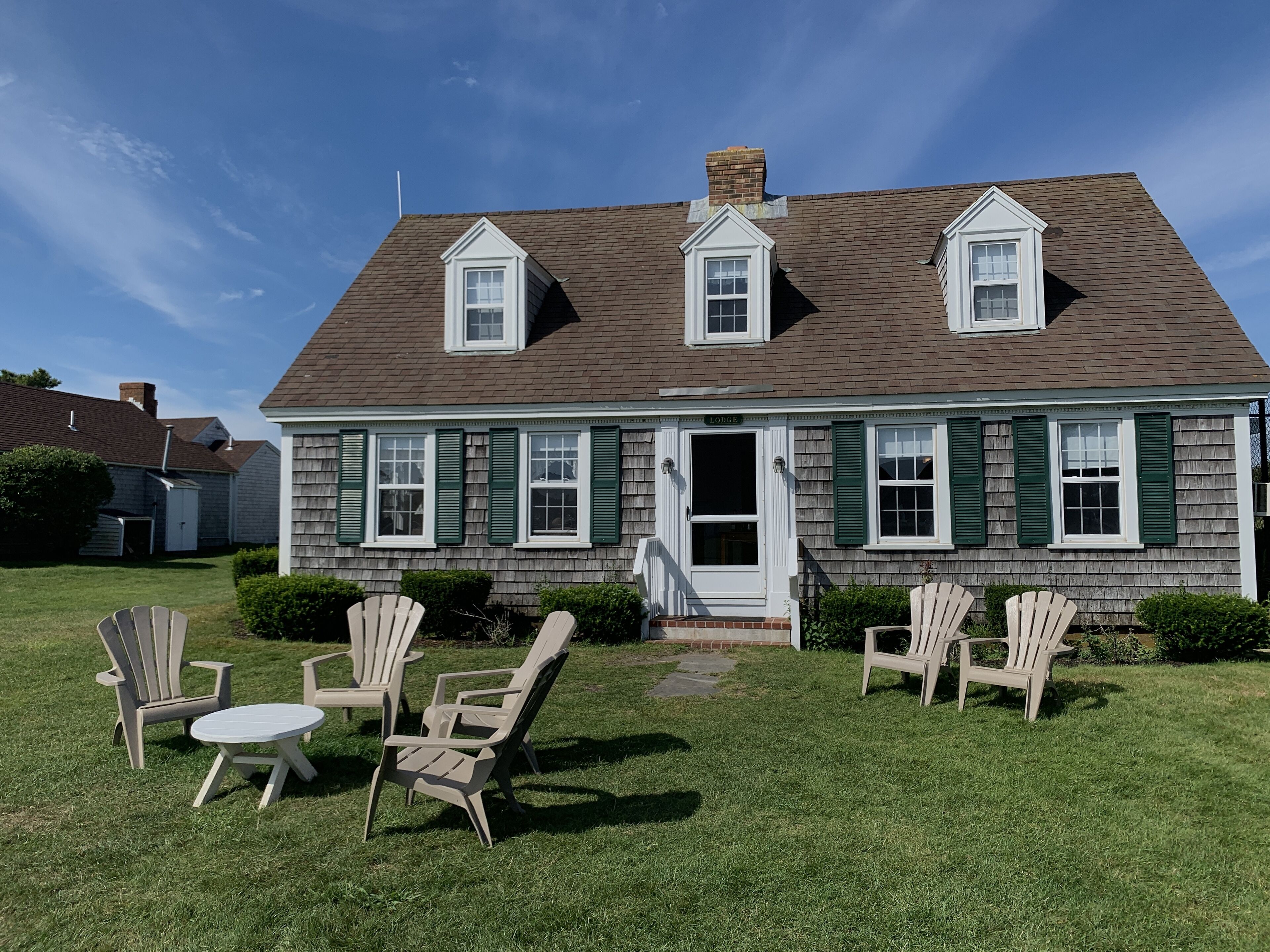 A two-story house with a front porch, a chimney, and a small front yard with lawn chairs and a table.