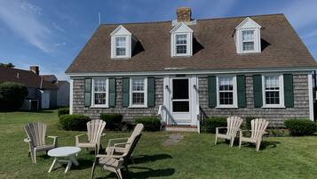A two-story house with a front porch, a chimney, and a small front yard with lawn chairs and a table.
