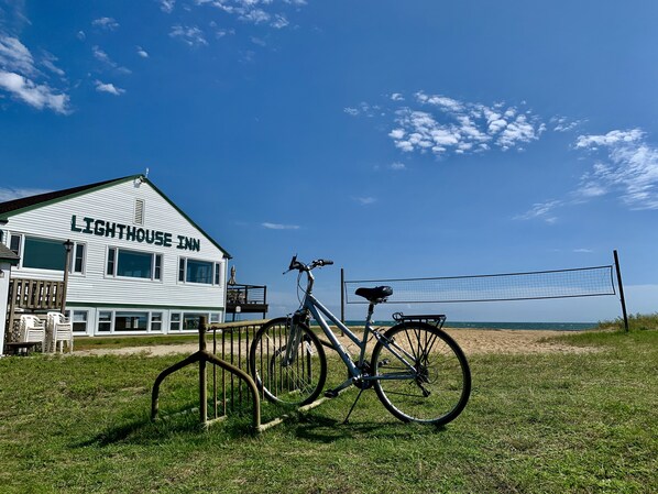 A white building with "LIGHTHOUSE INN" signage, a bicycle, and a volleyball net. - Lighthouse Inn (West Dennis)
