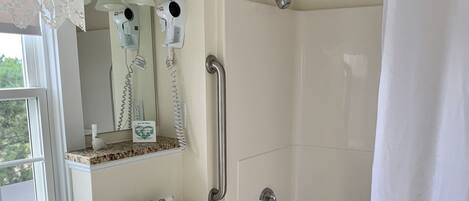 A bathroom with a sink, mirror, vanity, towel rack, shower, and toilet.