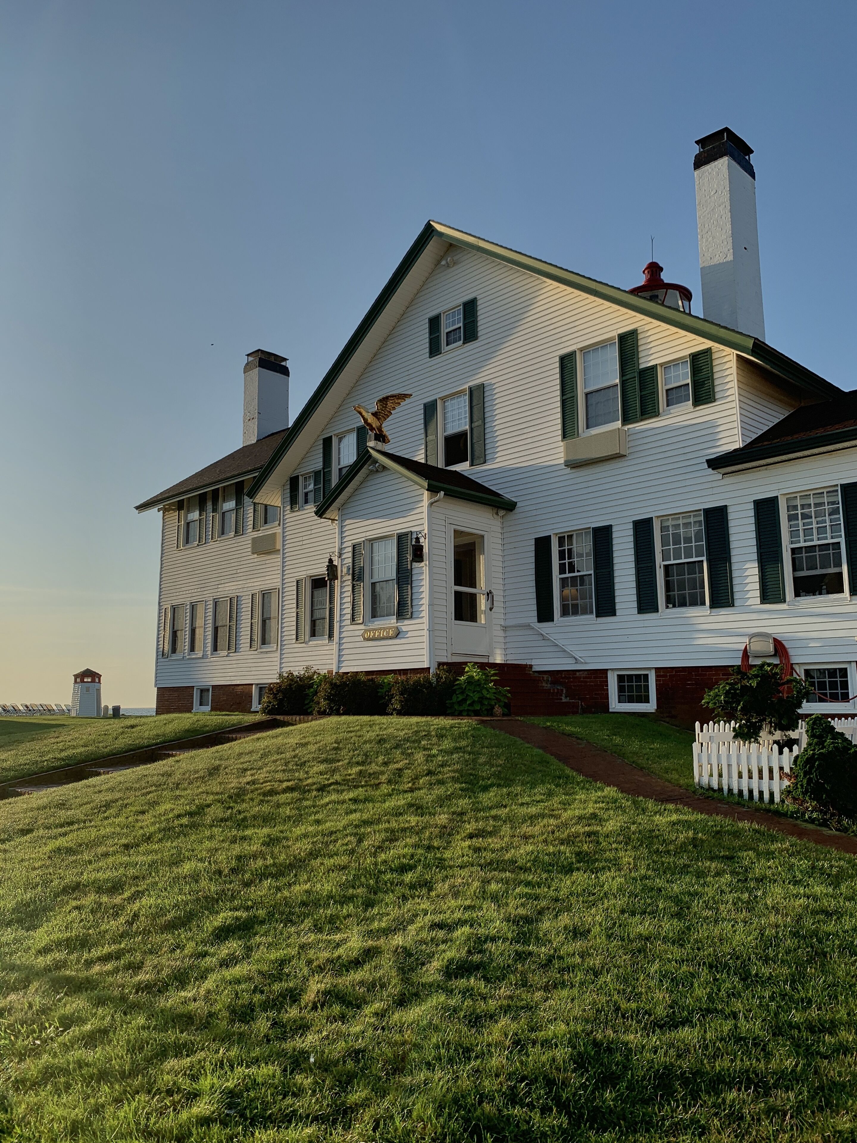 A large white house with green shutters, a chimney, and a small tower.